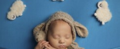 Newborn baby in blue blanket surrounded by knitted clouds