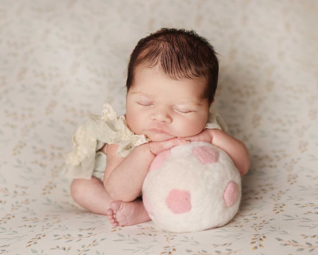 Newborn hugging a soft toy ball